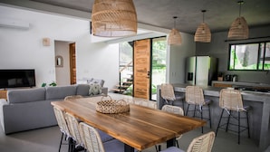 A modern kitchen with a wooden dining table, wicker chairs, and pendant lights.