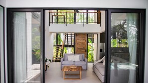 A modern living room with a sofa, a coffee table, and a balcony with a view of greenery.
