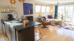 A modern kitchen with a central island, wooden shelves, and a dining area with a colorful rug. - Modern & Sunny House Steps from the Promenade. Private Parking! (Portland)