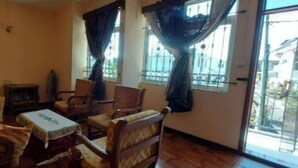 A living room with a sofa, armchairs, a small table, and a television. There are two windows with curtains, and a view of the outside is visible. - Villa Floreal 5 (floreal)