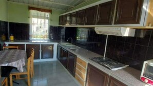 A kitchen with dark cabinets, a stove, and a microwave. There is a window with curtains and a table with chairs. - Villa Floreal 5 (floreal)