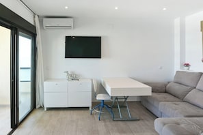 A modern living space with a white desk, a sofa, and a television mounted on the wall.