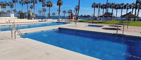Ein Schwimmbecken mit klarem, blauem Wasser, umgeben von Palmen und blauem Himmel.