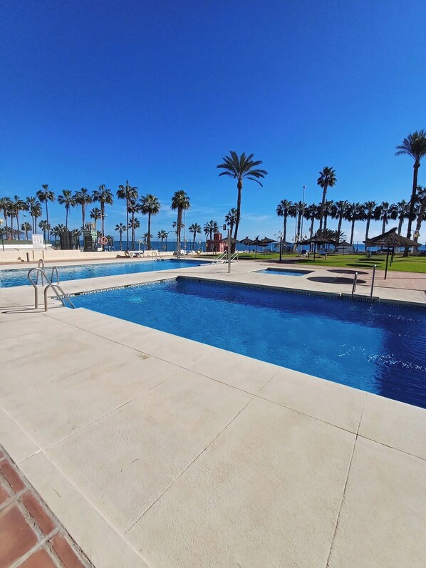 A swimming pool with clear blue water, surrounded by palm trees and a clear sky.