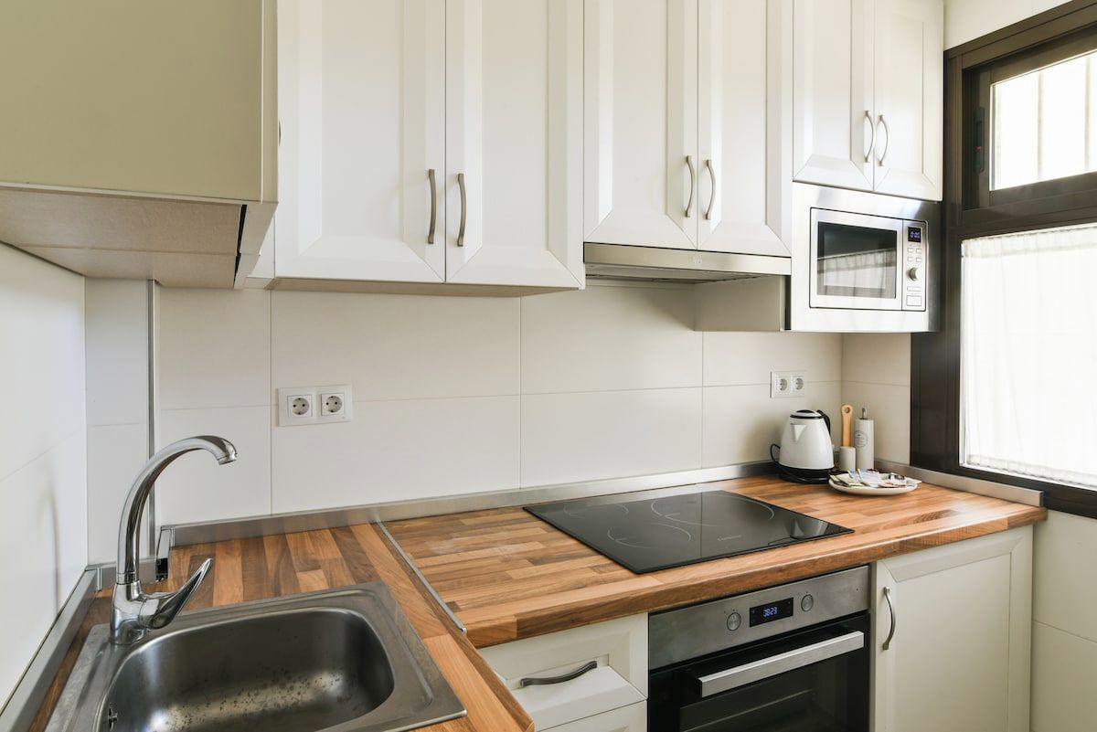 Een moderne keuken met witte kastjes, een roestvrijstalen spoelbak, een ingebouwde oven en een magnetron.