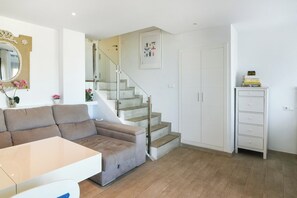 Una sala moderna con un sofá, una mesa de centro, una escalera y un armario blanco.