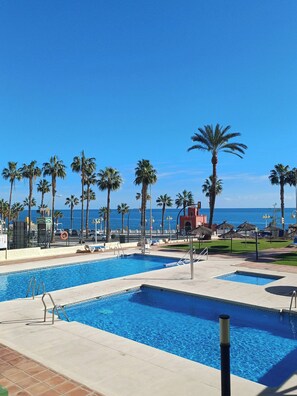 Zona de piscina con agua cristalina y azul, rodeada de palmeras y vista al océano.