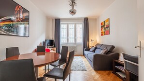 A modern living room with a dining area, a sofa, a TV, and artwork on the walls. - Le Kléber  - Appt en hypercentre, proche Place Kléber (Strasbourg)