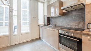 A modern kitchen with a built-in oven, a stainless steel range hood, and a large window. - Le Kléber  - Appt en hypercentre, proche Place Kléber (Strasbourg)