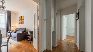 A modern living room with a grey sofa, wooden herringbone flooring, and a large window with curtains. - Le Kléber  - Appt en hypercentre, proche Place Kléber (Strasbourg)