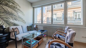 Una sala de estar moderna con sofá, sillones, una mesa de centro de vidrio y un ventanal con vistas a edificios.