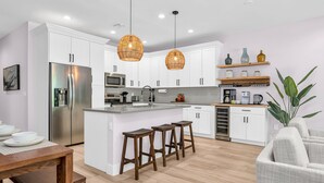 A modern kitchen with white cabinets, stainless steel appliances, and a central island with stools. - Jupiter Palms Oasis | Luxe Pool/Spa Table Tennis! (Jupiter)