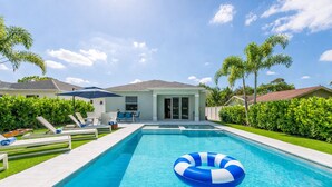 A swimming pool with lounge chairs and a house in the background. - Jupiter Palms Oasis | Luxe Pool/Spa Table Tennis! (Jupiter)