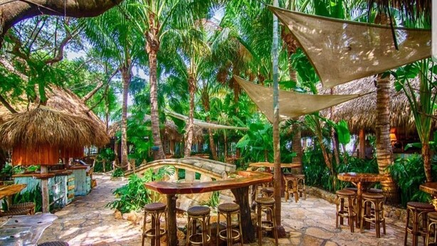 An outdoor restaurant area with stone flooring, wooden tables, and thatched-roof structures. - Jupiter Palms Oasis | Luxe Pool/Spa Table Tennis! (Jupiter)