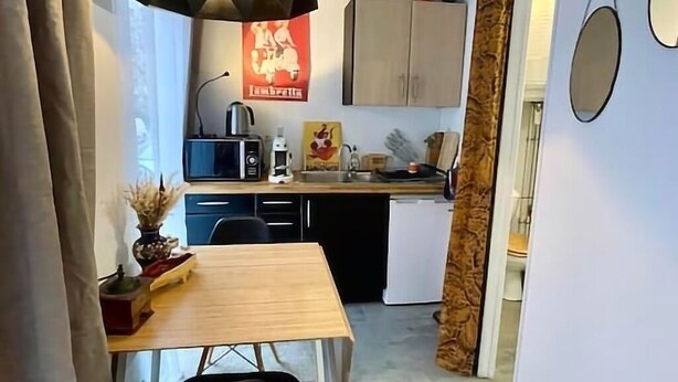 Una cucina compatta con zona pranzo, una lampada a sospensione nera e un poster rosso appeso al muro.