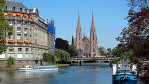 Un edificio storico con una grande cattedrale sullo sfondo, un fiume con barche e un ponte.