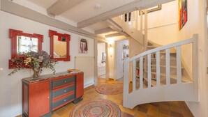 Un pasillo con una escalera de madera, un armario rojo con cajones y dos alfombras circulares en el suelo.