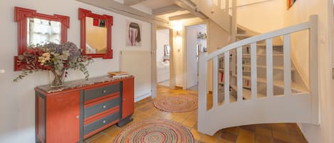 A hallway with a wooden staircase, a red cabinet with drawers, and two circular rugs on the floor.
