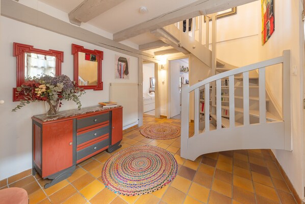 Un couloir avec un escalier en bois, un meuble rouge avec des tiroirs et deux tapis ronds sur le sol.