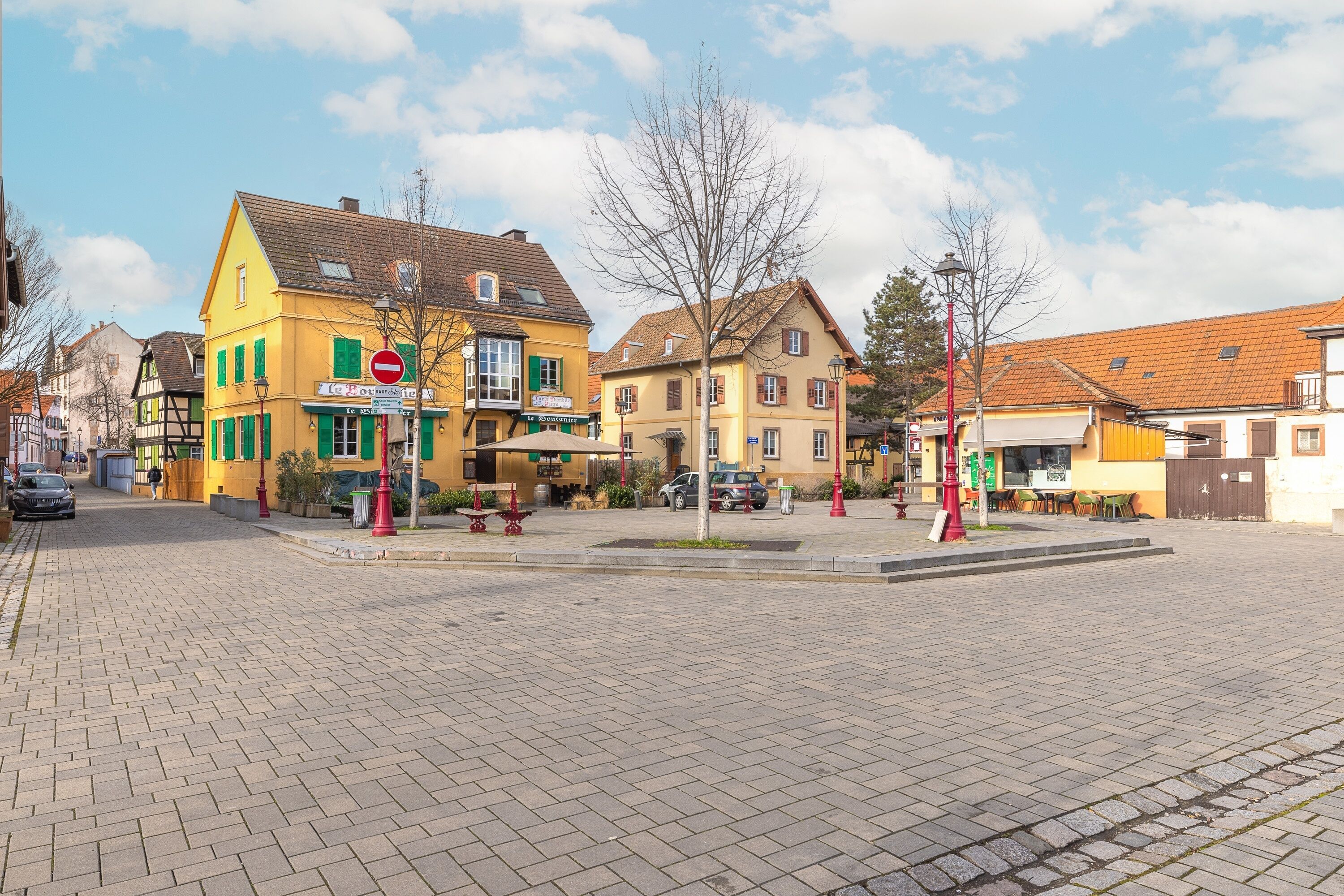A cobblestone street with historic buildings, a no entry sign, and a small plaza with seating.
