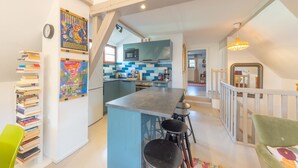 Una cocina moderna con una isla central, taburetes de bar y un área de comedor con una silla verde.