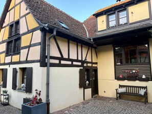 A traditional half-timbered building with a sloped roof, a bench outside, and a small garden area with potted plants.