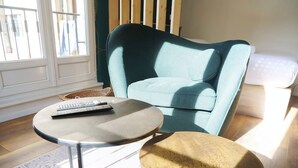 A room with a teal armchair, a round table with a remote control, and a small stool. - Le Cocon Urbain - Joli Studio récemment rénové (Strasbourg)