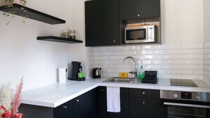 A modern kitchen with black cabinets, a white countertop, a microwave, a coffee maker, and an oven. - Le Cocon Urbain - Joli Studio récemment rénové (Strasbourg)