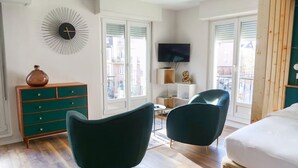 A modern bedroom with a bed, two green armchairs, a wooden dresser, a TV, and a decorative clock on the wall. - Le Cocon Urbain - Joli Studio récemment rénové (Strasbourg)