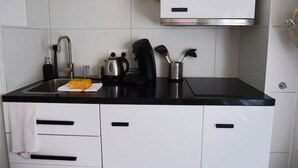 Une cuisine avec des meubles blancs, un plan de travail noir, un évier en acier inoxydable, une bouilloire, une machine à café et un porte-ustensiles.