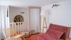Une pièce avec un canapé rose, un fauteuil en osier, une petite table, un tapis blanc, un miroir et une lampe.