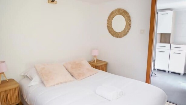 Une chambre à coucher avec un lit, une table de chevet avec une lampe, un miroir rond accroché au mur et une armoire à l’arrière-plan.