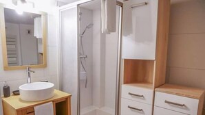 Une salle de bain moderne avec un lavabo blanc, un miroir et une cabine de douche.