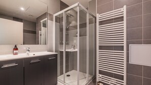 A modern bathroom with a glass-enclosed shower, a white sink, and a towel rack.