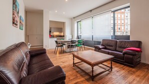 A modern living room with a brown leather sofa, a wooden coffee table, and a dining area with green chairs.