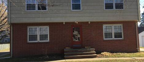 A two-story house with a red front door, a brick facade, and a small front porch.