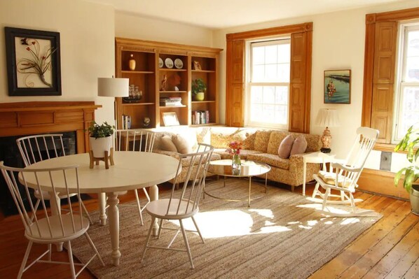 A cozy living room with a fireplace, a round dining table with chairs, a sofa, and a bookshelf.
