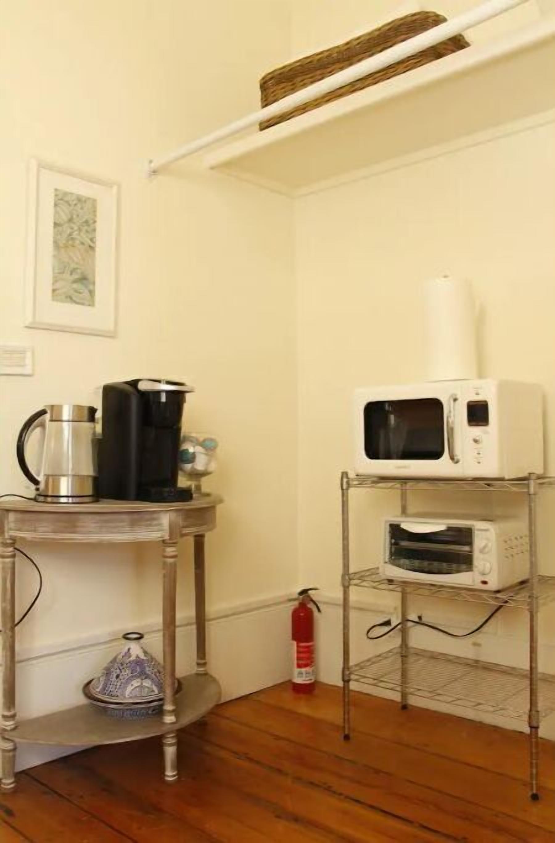 A kitchenette with a coffee maker, microwave, and toaster on shelves, a small table with a decorative item, and a fire extinguisher on the floor.