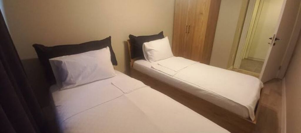 A small, single-room hotel room with two single beds, a wooden wardrobe, and a door leading to a bathroom.