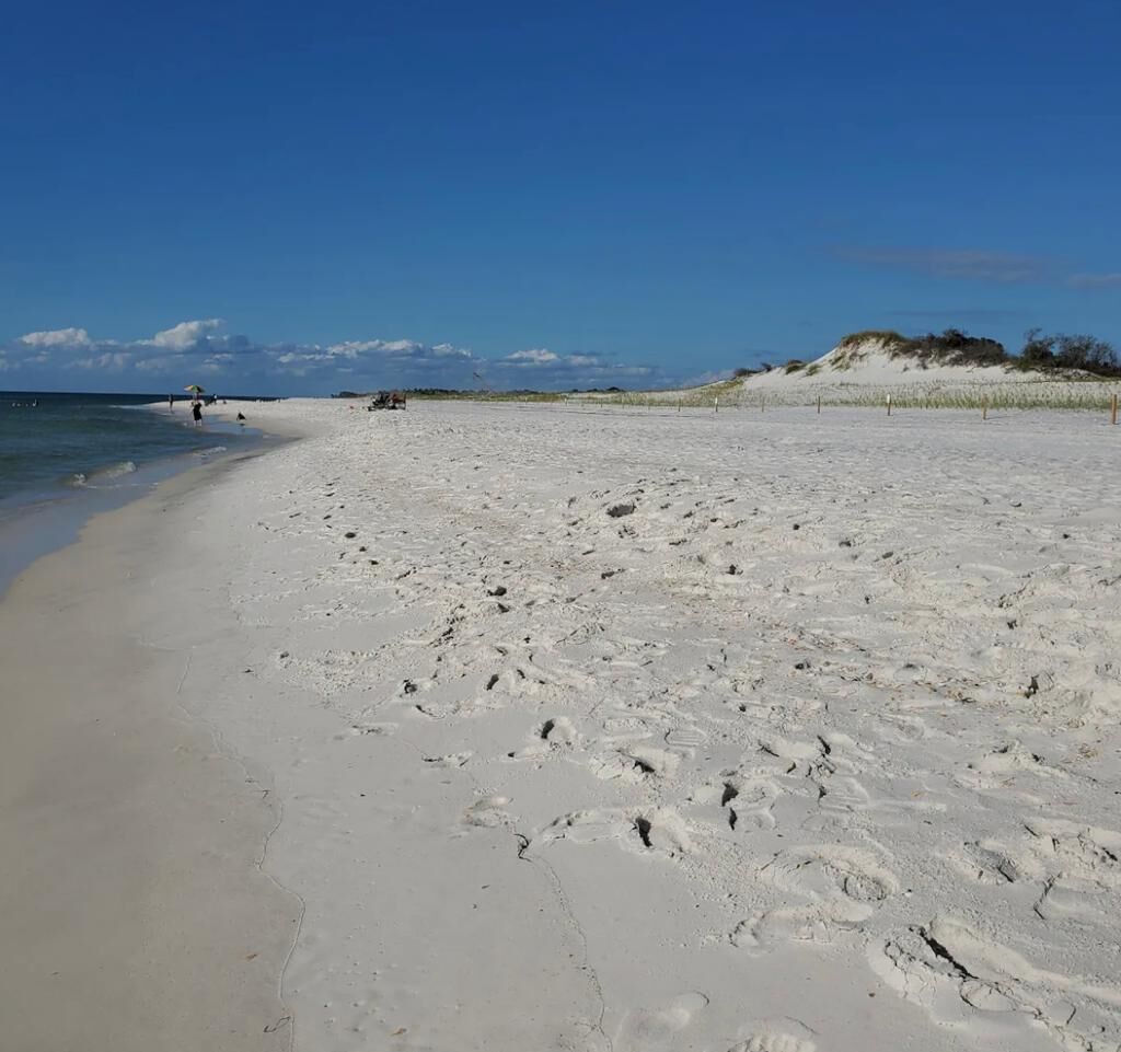 A wide sandy beach with footprints, a clear blue sky, and a distant dune.