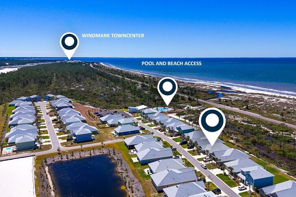 Ein Luftbild eines Wohngebiets mit Pool und Zugang zum Strand, das moderne Häuser mit Satteldächern und ein zentrales Stadtzentrum zeigt.