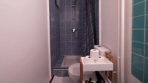 A small bathroom with a shower, toilet, and a shelf with toiletries.