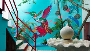 A staircase with red railings leading to a room with a colorful mural of a bird and a decorative stone fountain. - Linda Vecindad Playa del Carmen (Playa del Carmen)
