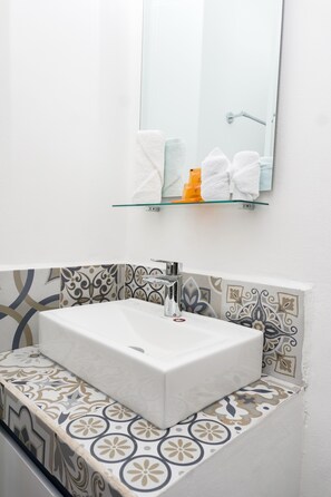 A bathroom with a white sink, a glass shelf above it, and patterned tiles on the walls. - Linda Vecindad Playa del Carmen (Playa del Carmen)