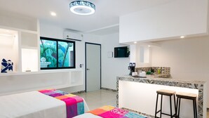 A hotel room with two beds, a small kitchenette, a TV mounted on the wall, and a window with a view of palm trees. - Linda Vecindad Playa del Carmen (Playa del Carmen)