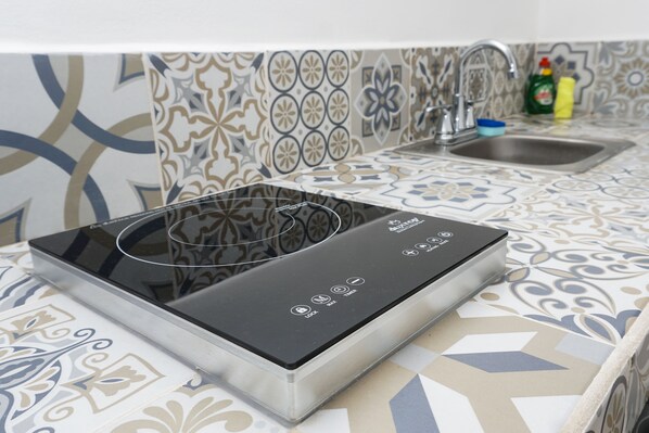A kitchen with a modern induction cooktop, a stainless steel sink, and patterned backsplash tiles. - Linda Vecindad Playa del Carmen (Playa del Carmen)