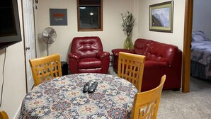 A room with a round table, two red leather chairs, a red sofa, a TV mounted on the wall, a window, and a door leading to another room. - 305 2bd Lower · Moose 2 bedroom lower, close to downtown (Fairbanks)