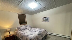 A bedroom with a bed, a nightstand, a lamp, a picture on the wall, and a ceiling light. - 305 2bd Lower · Moose 2 bedroom lower, close to downtown (Fairbanks)