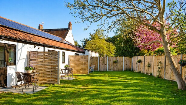 A residential backyard with a patio, a wooden fence, and a tree with pink blossoms. - Lodge 6 - Lytton Tree Lodge - Reydon (Reydon)