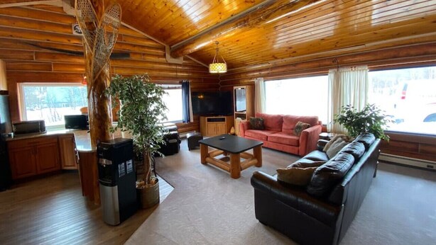 A spacious living area with a wooden ceiling, a sofa set, a coffee table, and a television. - 2010 Steese Hwy · Aurora viewing, quiet space, entire log home (Fairbanks)